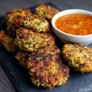 Crunchy quinoa veggie patties stacked on a plate, golden brown with fresh herbs and served with dipping sauce.
