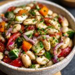 A vibrant bowl of marinated za’atar bean salad with white beans, cherry tomatoes, red onion, and fresh herbs.