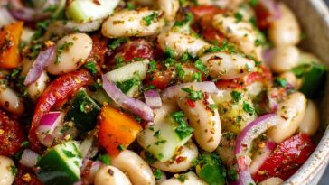 A vibrant bowl of marinated za’atar bean salad with white beans, cherry tomatoes, red onion, and fresh herbs.