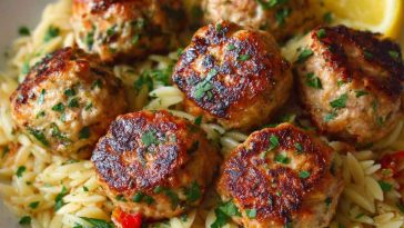 Greek chicken meatballs served over lemon orzo pasta, garnished with fresh herbs and feta cheese.