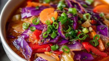 Bowl of cabbage fat burning soup with carrots, celery, and tomatoes, garnished with fresh parsley.