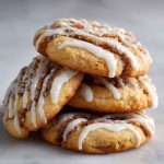 Swirled cinnamon roll cookies drizzled with vanilla glaze on a cooling rack.