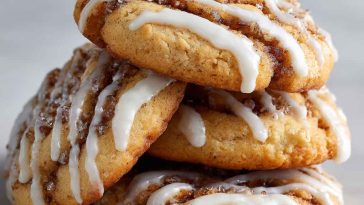 Swirled cinnamon roll cookies drizzled with vanilla glaze on a cooling rack.