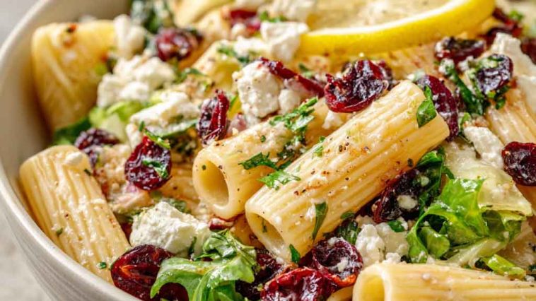 A vibrant bowl of rigatoni pasta tossed with feta cheese, dried cranberries, fresh herbs, and lemon vinaigrette.