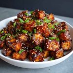 Crispy honey garlic tofu bites glazed with sticky sauce, garnished with sesame seeds and green onions.