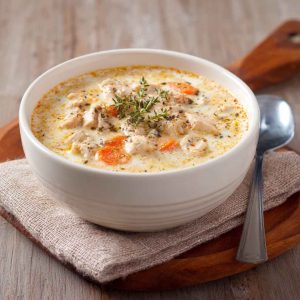 A bowl of creamy cottage cheese chicken soup with shredded chicken, herbs, and a swirl of cottage cheese, served with crusty bread.