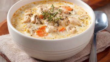 A bowl of creamy cottage cheese chicken soup with shredded chicken, herbs, and a swirl of cottage cheese, served with crusty bread.
