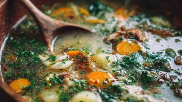 A steaming bowl of Italian Penicillin Soup with shredded chicken, pastina pasta, carrots, and fresh herbs in a golden broth.