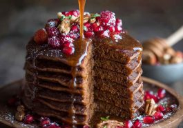 Stack of gingerbread pancakes topped with whipped cream, syrup, and a sprinkle of cinnamon.