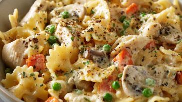 A creamy bowl of chicken pot pie pasta with shredded chicken, peas, carrots, and rotini noodles in a rich sauce.