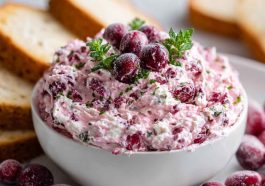 A creamy block of cranberry cream cheese spread topped with ruby-red cranberry sauce and fresh rosemary, served with crackers.
