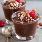 Glass jar of healthy chocolate pudding topped with berries and a sprinkle of cacao nibs.