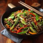 A skillet filled with ground beef stir fry, colorful bell peppers, broccoli, and sesame seeds in a savory sauce.