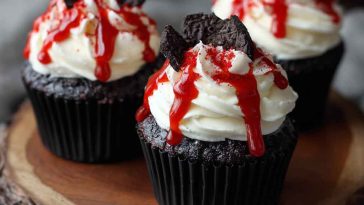 Halloween vampire bite cupcakes with white frosting, red filling oozing from fang marks, and spooky decor.