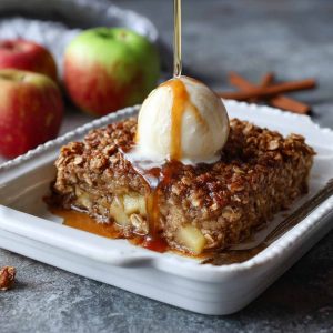 Baked oatmeal with apple chunks and cinnamon in a rustic dish, topped with oats and golden edges.