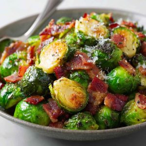 Roasted Brussels sprouts tossed with crispy bacon pieces, garlic, and herbs, served hot on a rustic plate.