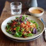 Crispy rice salad tossed with fresh vegetables, herbs, and drizzled with spicy peanut-chili dressing served in a vibrant bowl.
