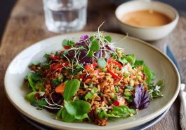 Crispy rice salad tossed with fresh vegetables, herbs, and drizzled with spicy peanut-chili dressing served in a vibrant bowl.