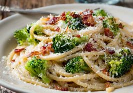 Creamy bucatini pasta tossed with melted cheese, crispy maple bacon, and tender broccoli florets served in a rustic bowl.