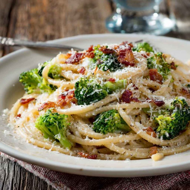 Creamy bucatini pasta tossed with melted cheese, crispy maple bacon, and tender broccoli florets served in a rustic bowl.