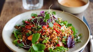 Crispy rice salad tossed with fresh vegetables, herbs, and drizzled with spicy peanut-chili dressing served in a vibrant bowl.