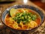 Red curry wonton soup with tender wontons in a spicy coconut curry broth, garnished with fresh herbs.