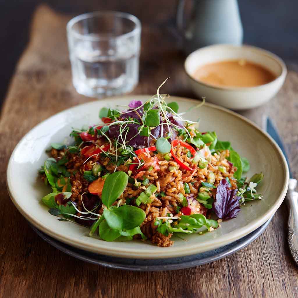 Crispy rice salad tossed with fresh vegetables, herbs, and drizzled with spicy peanut-chili dressing served in a vibrant bowl.