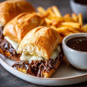 Slow cooker French dip sandwiches with tender beef, melted cheese, and toasted hoagie rolls served with au jus dipping sauce.