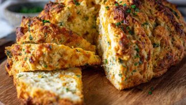 Loaf of golden cheddar and herb soda bread sliced on a wooden board.