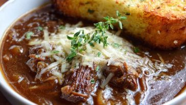 Rich French onion short rib soup topped with golden Gruyère cheese toast served in a rustic bowl.