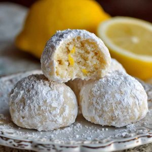 Bright and buttery lemon cream snowball cookies dusted with powdered sugar, stacked on a festive holiday plate.