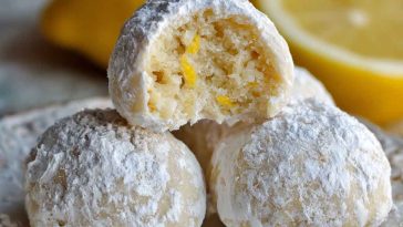 Bright and buttery lemon cream snowball cookies dusted with powdered sugar, stacked on a festive holiday plate.