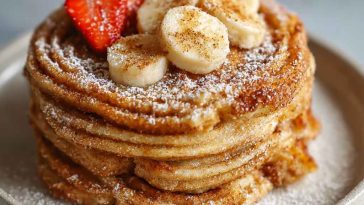 Stack of irresistible Spanish churro pancakes dusted with cinnamon sugar, drizzled with chocolate sauce, and served warm.