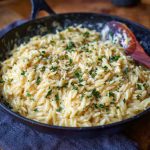 "A bowl of creamy garlic parmesan orzo pasta garnished with fresh parsley and grated cheese."