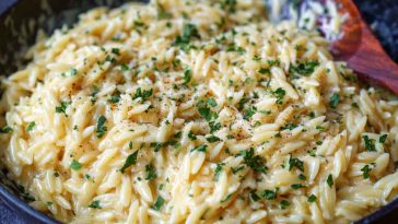 "A bowl of creamy garlic parmesan orzo pasta garnished with fresh parsley and grated cheese."