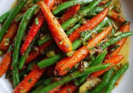 "A colorful dish of honey glazed carrots and green beans garnished with sesame seeds and fresh herbs."