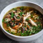 "A comforting bowl of rotisserie chicken and mushroom soup garnished with fresh herbs and served warm."