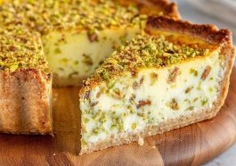 Slice of baked pistachio custard pie topped with whipped cream and crushed pistachios