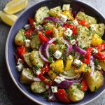 Colorful Greek potato salad with fresh herbs, olives, red onion, and lemon vinaigrette served in a rustic bowl.