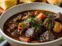 Rustic French-style beef stew simmered in red wine with carrots, onions, and herbs served in a cast-iron pot.