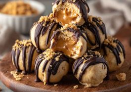 No-bake peanut butter cheesecake balls coated in chocolate and drizzled with peanut butter, served on a dessert tray.