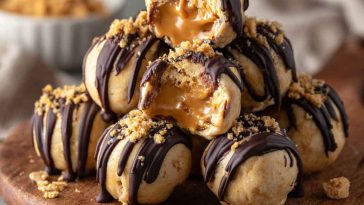 No-bake peanut butter cheesecake balls coated in chocolate and drizzled with peanut butter, served on a dessert tray.