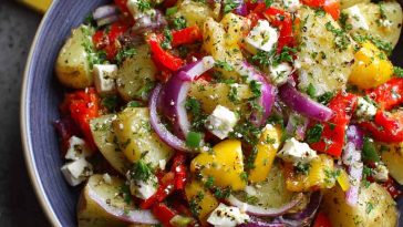 Colorful Greek potato salad with fresh herbs, olives, red onion, and lemon vinaigrette served in a rustic bowl.