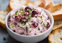 Bowl of cranberry jalapeño cream cheese dip garnished with fresh herbs