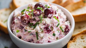 Bowl of cranberry jalapeño cream cheese dip garnished with fresh herbs