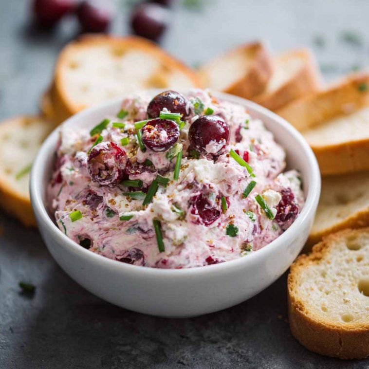 Bowl of cranberry jalapeño cream cheese dip garnished with fresh herbs