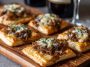 Mini French onion tarts made with golden puff pastry, caramelized onions, and melted Gruyère cheese served on a rustic platter.
