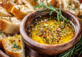 Rustic bowl of loaded bread dipping oil with olive oil, garlic, herbs, and spices served alongside crusty bread slices.