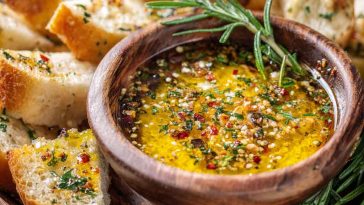 Rustic bowl of loaded bread dipping oil with olive oil, garlic, herbs, and spices served alongside crusty bread slices.