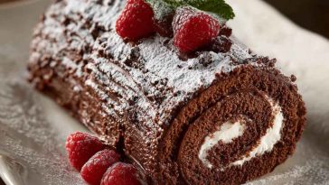Traditional chocolate Yule log cake dusted with powdered sugar and decorated with holly leaves.